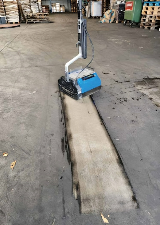 Heavy-duty floor scrubber machine cleaning dirty warehouse concrete surface with visible clean track.