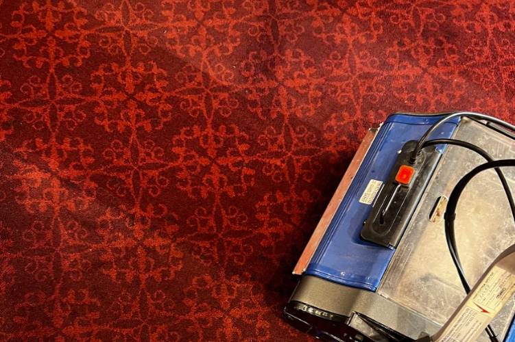 Professional carpet floor cleaning with a commercial scrubber on patterned red carpet in a hotel or venue.
