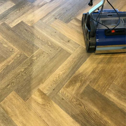 Commercial floor scrubber cleaning a timber herringbone floor, showing clear contrast between cleaned and dirty sections.